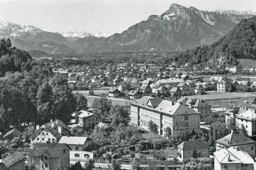 © Ansichtskarte vom Ende der 1950er-Jahre, Archiv Mayr
Wie auf dieser Fotografie der 1950er-Jahre wird auch heute noch der Stadtteil Gnigl vom Schulensemble von 1927/28 dominiert. Architekt Paul Geppert der Ältere hat die Schule und die beiden Lehrerwohnhäuser um ein platzartiges Zentrum gruppiert. Der Gestaltungsbeirat bedauert den Gesamtabriss, macht sich angesichts der fortgeschrittenen Planung zum „Bildungscampus“ immerhin für die Erhaltung des im Bild ganz rechts erkennbaren Lehrerhauses stark. Wie auf dieser Fotografie der 1950er-Jahre wird auch heute noch der Stadtteil Gnigl vom Schulensemble von 1927/28 dominiert. Architekt Paul Geppert der Ältere hat die Schule und die beiden Lehrerwohnhäuser um ein platzartiges Zentrum gruppiert. Der Gestaltungsbeirat bedauert den Gesamtabriss, macht sich angesichts der fortgeschrittenen Planung zum „Bildungscampus“ immerhin für die Erhaltung des im Bild ganz rechts erkennbaren Lehrerhauses stark.