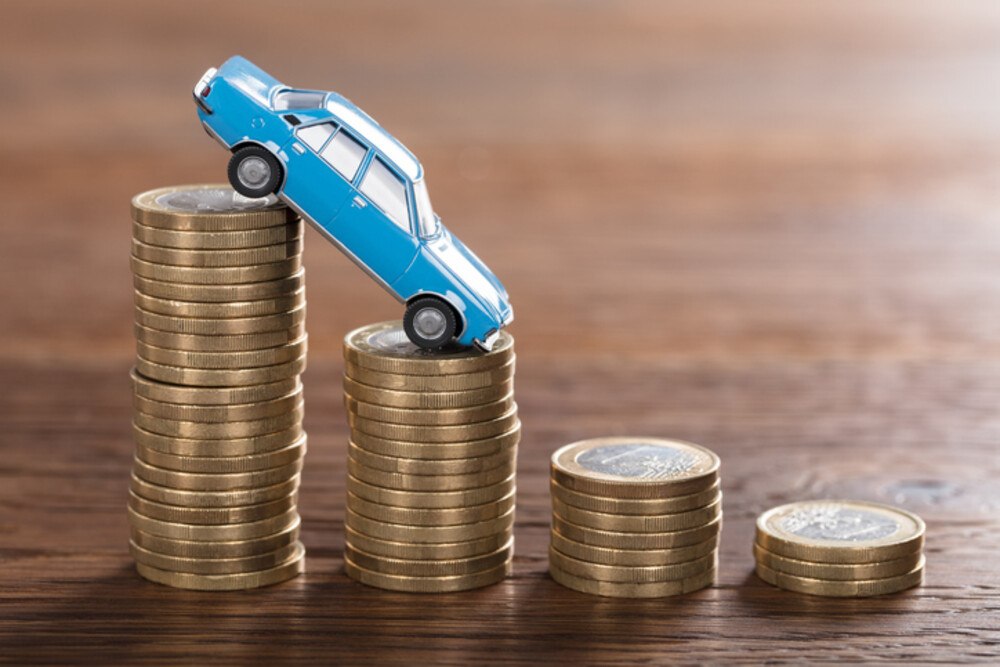 © AndreyPopov iStock / Getty Images Plus Automodell fällt von hohem Münzenstapel auf niedrigeren