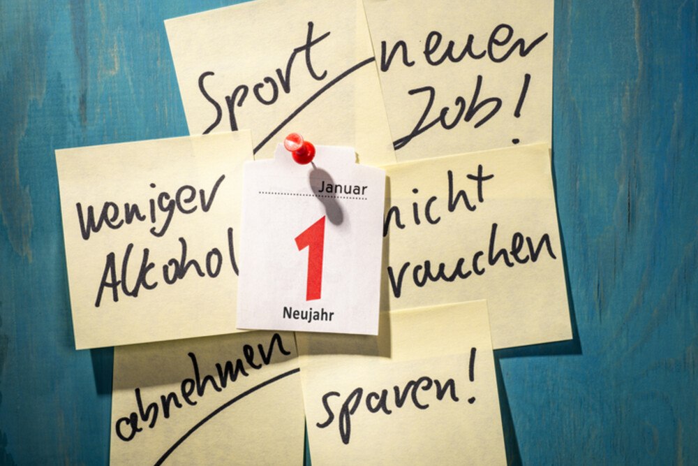© iStock / Getty Images Plus / gopixa
Der Jahreswechsel ist traditionell die Zeit der guten Vorsätze: Vielleicht das Rauchen aufgeben, mehr Sport treiben oder einfach nur weniger Süßes essen, sind einige der Klassiker.
Das Kalenderblatt des ersten Januars ist auf eine blaue Wand aufgepinnt. Rundherum hängen Post-its mit Neujahrsvorsätzen.
