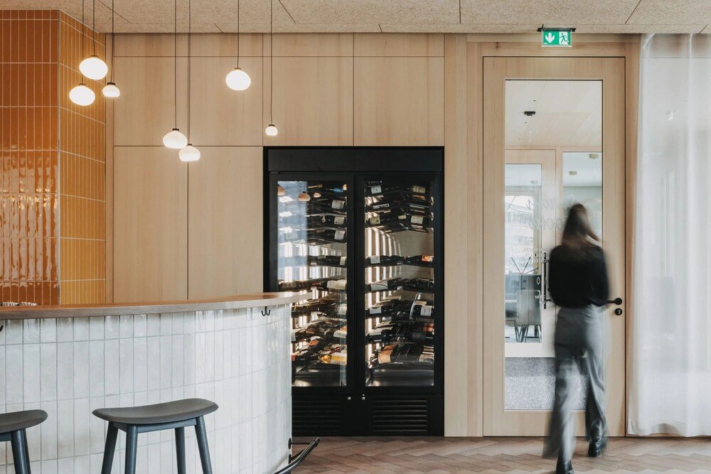 Fotografie des Innenbereichs des neuen, modern gestalteten Posthus in Egg. Links eine Bar, in der Mitte ein Weinkühlschrank. Viel helles Holz.