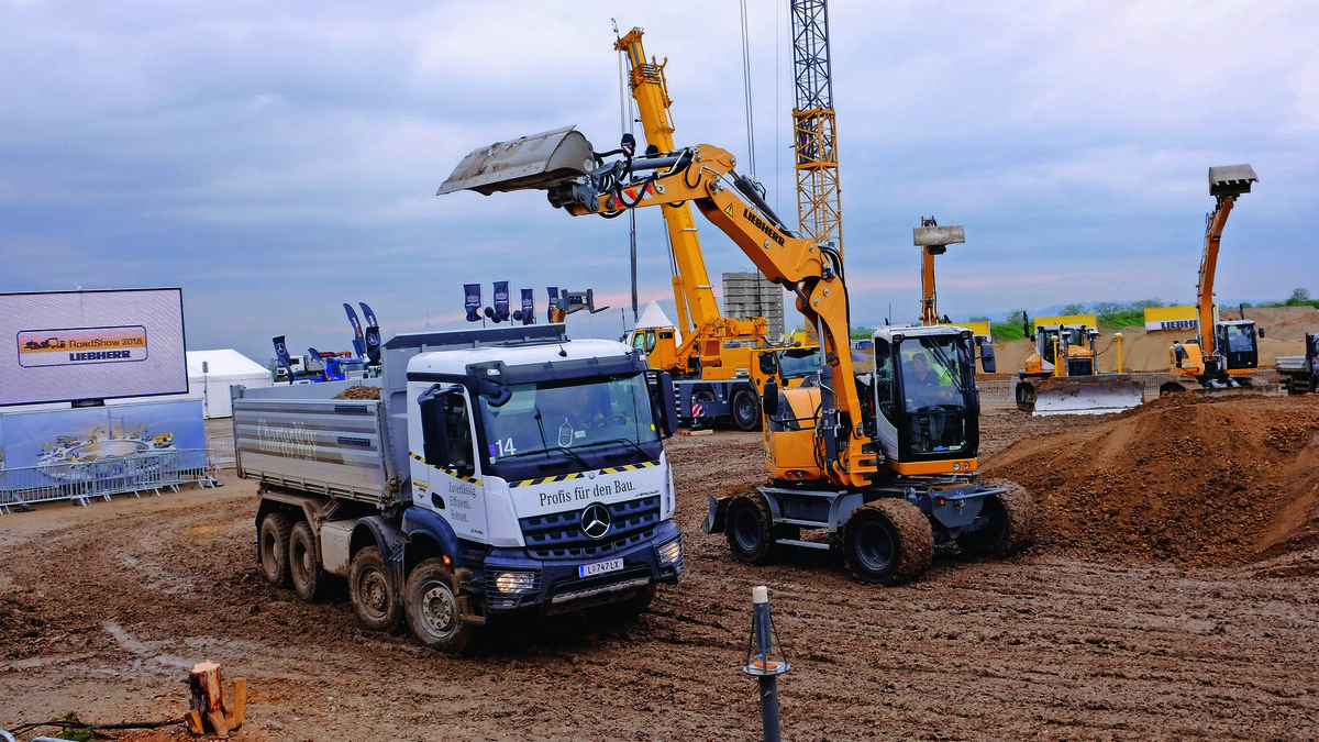 Mobilbagger A 912 Compact Litronic bei der Arbeit in dunklem, feuchtem Sand bei wolkigem Himmel