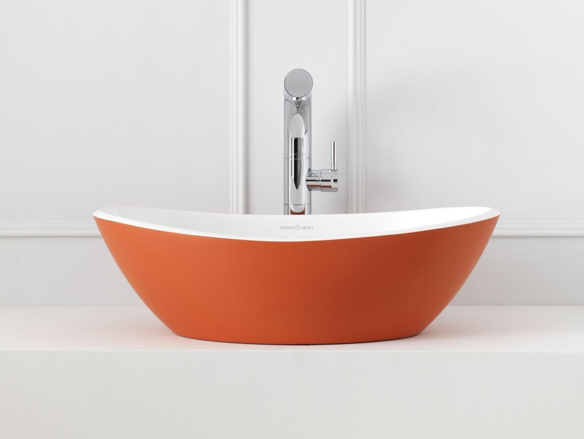 Das Waschbecken mit der orangen Außenfarbe hebt sich vom Weiß des restlichen Raumes ab