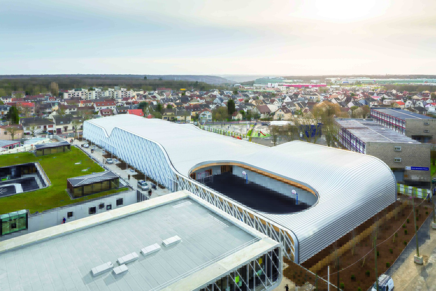 Ein Dach mit Hebungen und Senkungen überspannt kurvenreich das 130 Meter lange und 40 Meter breite Gebäude der neuen städtischen Sportanlage in Paris-Clamart (F). Über dem Leichtathletikbereich bleibt das Dach ausgespart.