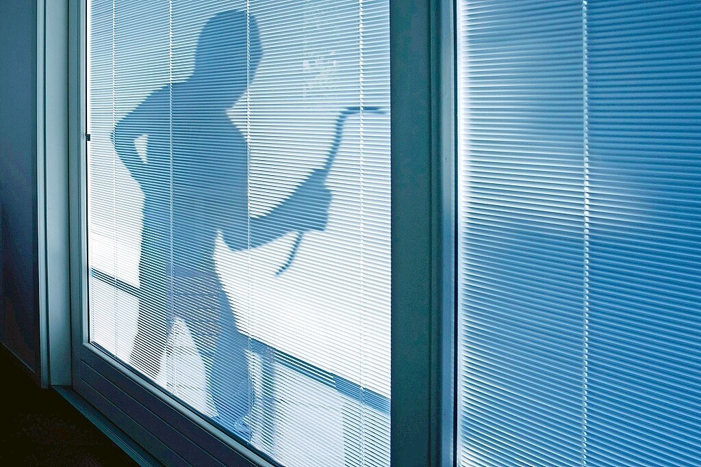 Der Schatten einer Person mit Brecheisen auf der Innenseite eines zugezonenen Rollos