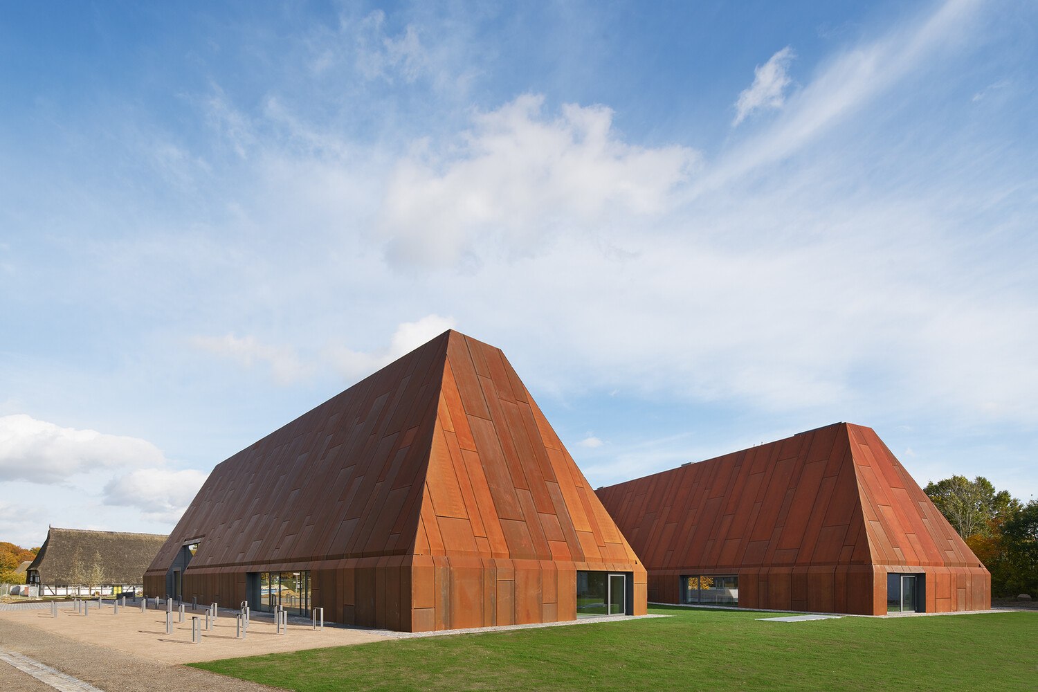 Die Neubauten für das Landesmuseum für Volkskunde im Museumsdorf Molfsee erinnern hinsichtlich ihrer Formgebung an regionale Bauernhäuser. Mit wetterfestem Baustahl einheitlich bekleidet werden Dach und Wand durch architektonische Transformation zur skulpturalen Großform, die Gebäude selbst zu Artefakten.