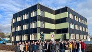 Eine Gruppe an Menschen steht vor einem grün-schwarzen Gebäude.