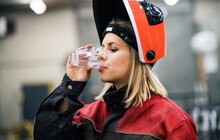 © Halfpoint iStock Gettyimages Plus Frau in Arbeitskleidung trinkt aus einem Wasserglas