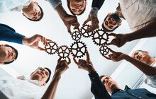 © NanoStockk iStock Getty Images Plus ein Team hält Zahnräder als Symbol