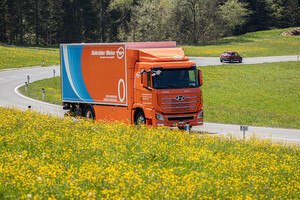 Ein Orangener Wasserstoff LKW bei Sonnenschein auf einer blumigen Landstraße