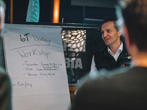 Ein Mann steht neben einem Whiteboard und hält einen Workshop für Besucher*innen.