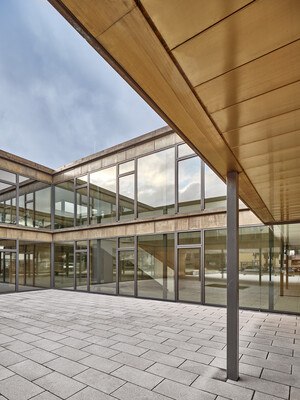 Durch die atriumähnliche Aussparung des Obergeschosses im Eingangsbereich entstehen zwei rechtwinklig zueinander liegende brückenartige Riegel, die auf Stahlstützen aufgeständert sind.