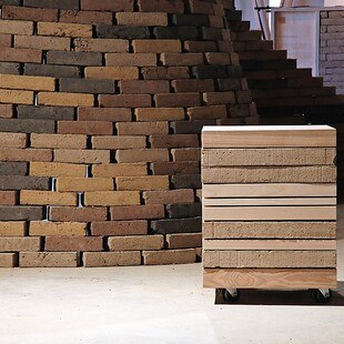 Wand mit Ziegel aus Lehm, davor steht ein Stapel von Lehm-Ziegeln