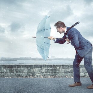 © photoschmidt iStock / Getty Images Plus Geschäftsmann mit Regenschirm im Gegenwind