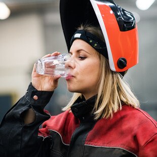 © Halfpoint iStock Gettyimages Plus Frau in Arbeitskleidung trinkt aus einem Wasserglas
