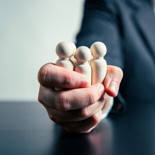 © Shutter2U iStock / Getty Images Plus Geschäftsperson hält Figuren fest in der Hand