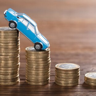 © AndreyPopov iStock / Getty Images Plus Automodell fällt von hohem Münzenstapel auf niedrigeren